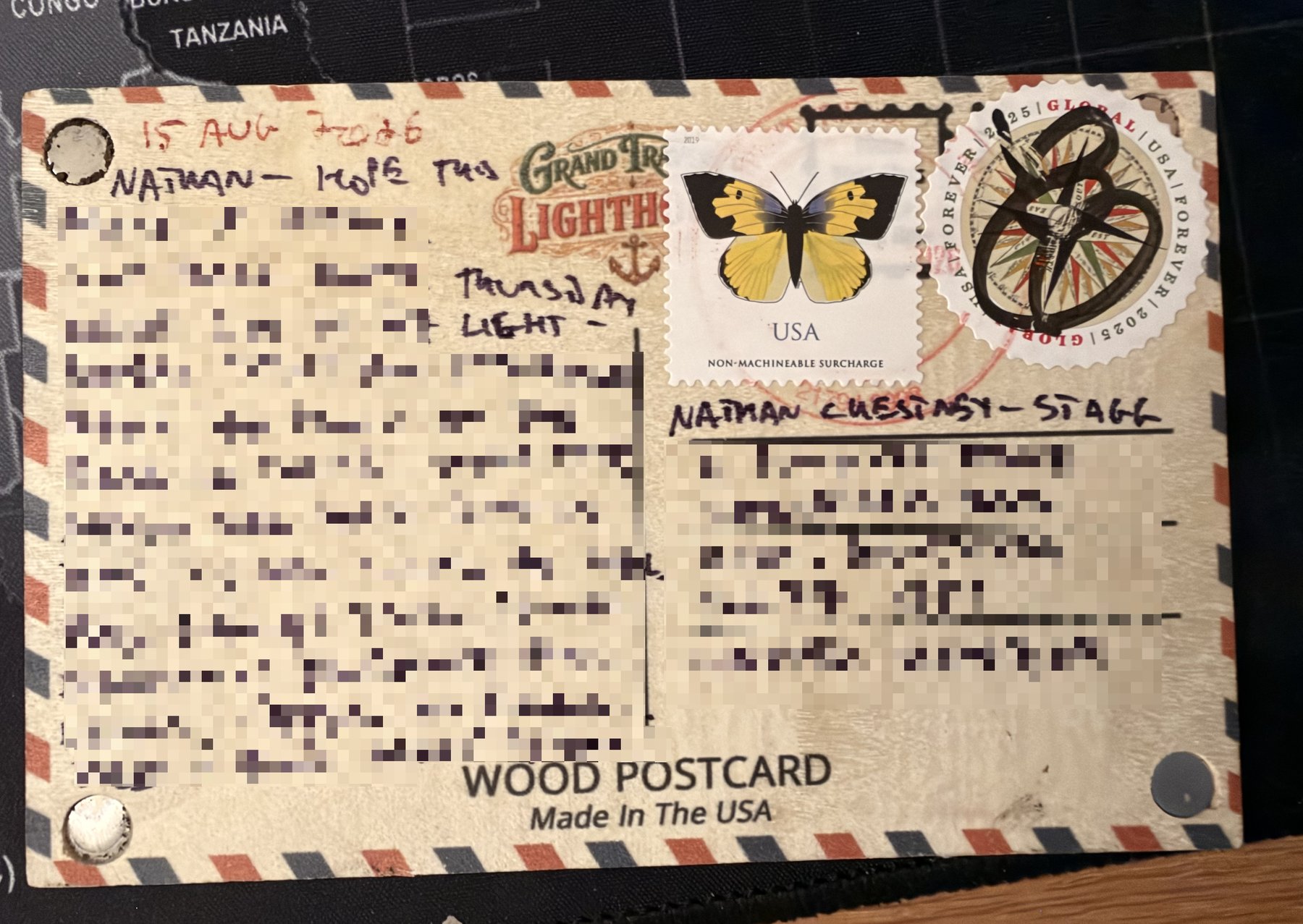 Wooden postcard back with airmail stripes, a yellow butterfly non-machineable surcharge stamp and a round Global Forever compass rose stamp cancelled by hand in black pen; message and address blurred