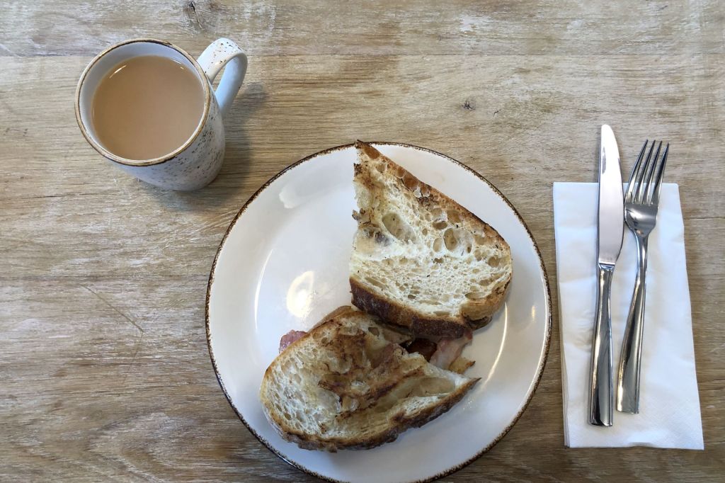 A mug of tea beside a plate of toasted sourdough with bacon on a wooden table